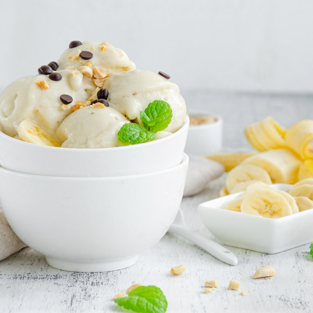 A bowl of banana ice cream next to a peeled banana