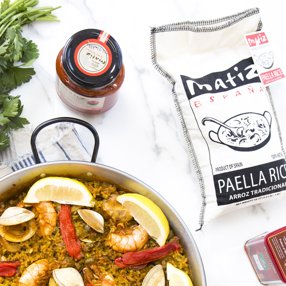 Bag of Matiz España traditional paella rice next to a pan of paella and a jar of sauce