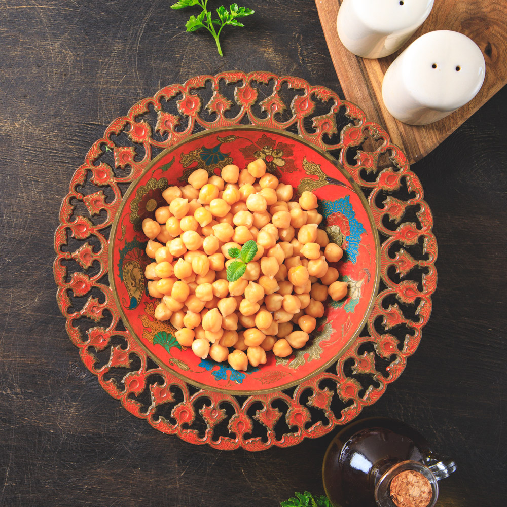 Cooked chick peas in a beautiful authentic plate next to a bottle of olive oil and salt and pepper shakers