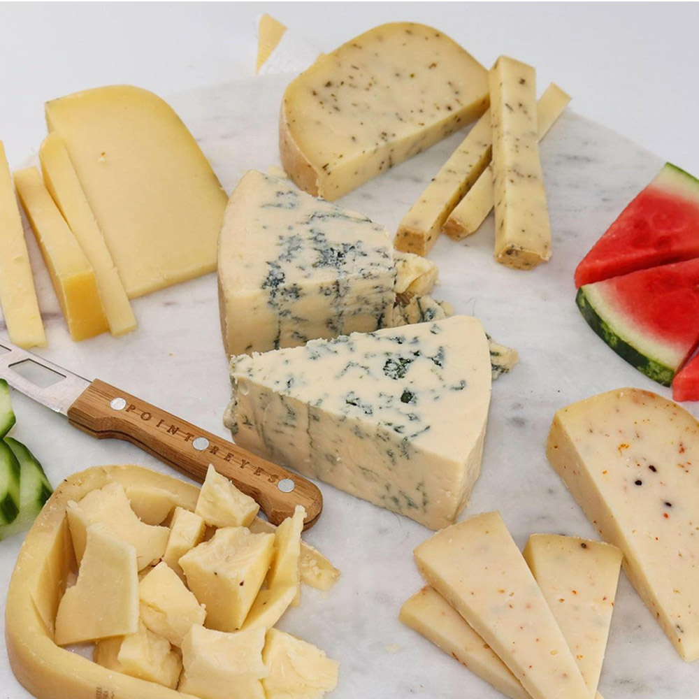 A cheese board with a few different kinds of cheeses and a cheese knife