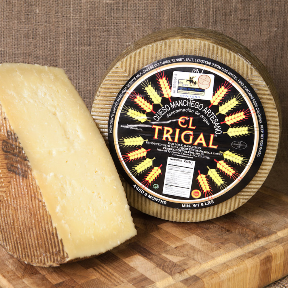 A wheel of manchego next to a half wheel of Manchego cheese on a wood board