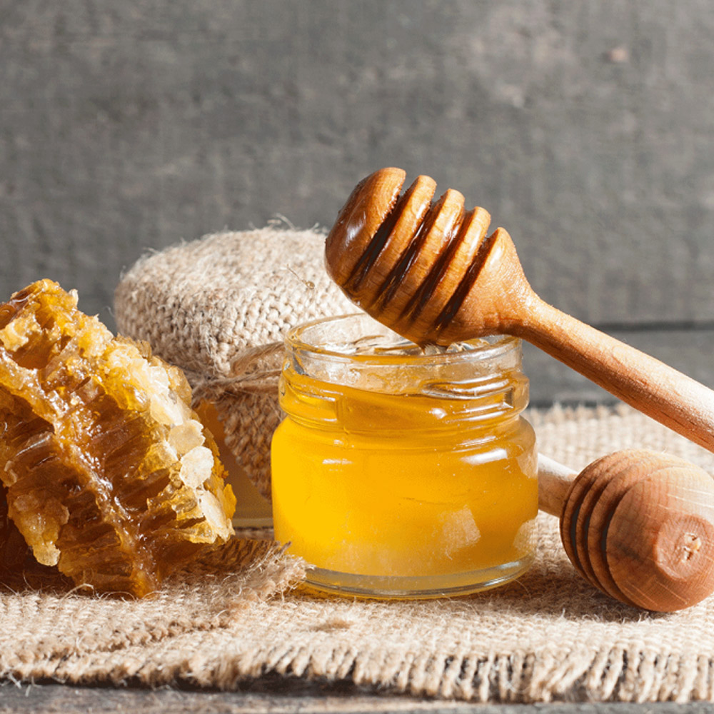 An open jar of honey with a honey stick