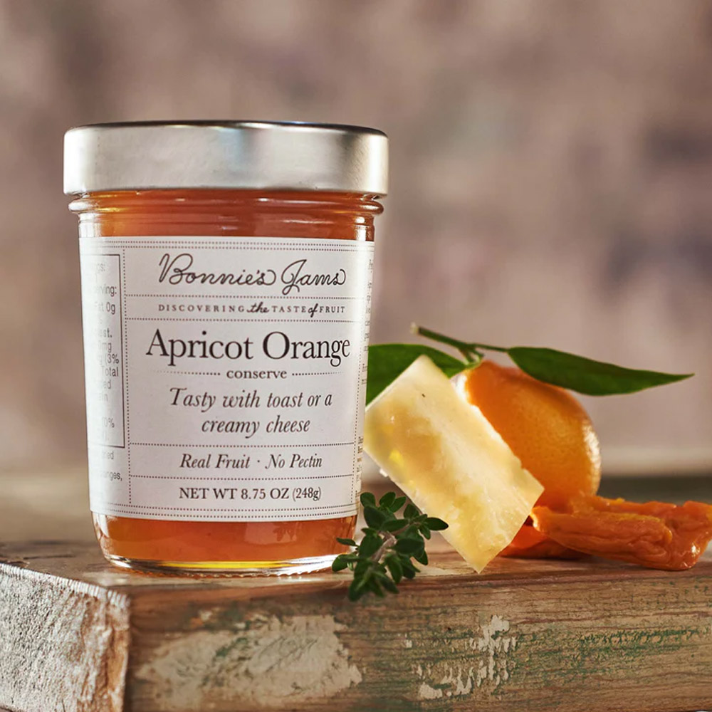 A jar of Bonnie's Jams Apricot Orange on a board next an orange and cheese
