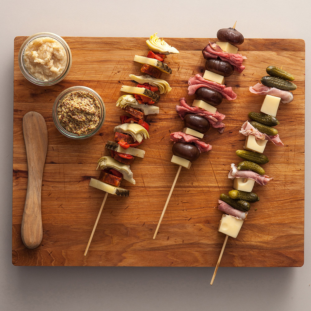 beaufor whole grain mustard in small cup with skewers of meats and cheeses and vegetables on cutting board