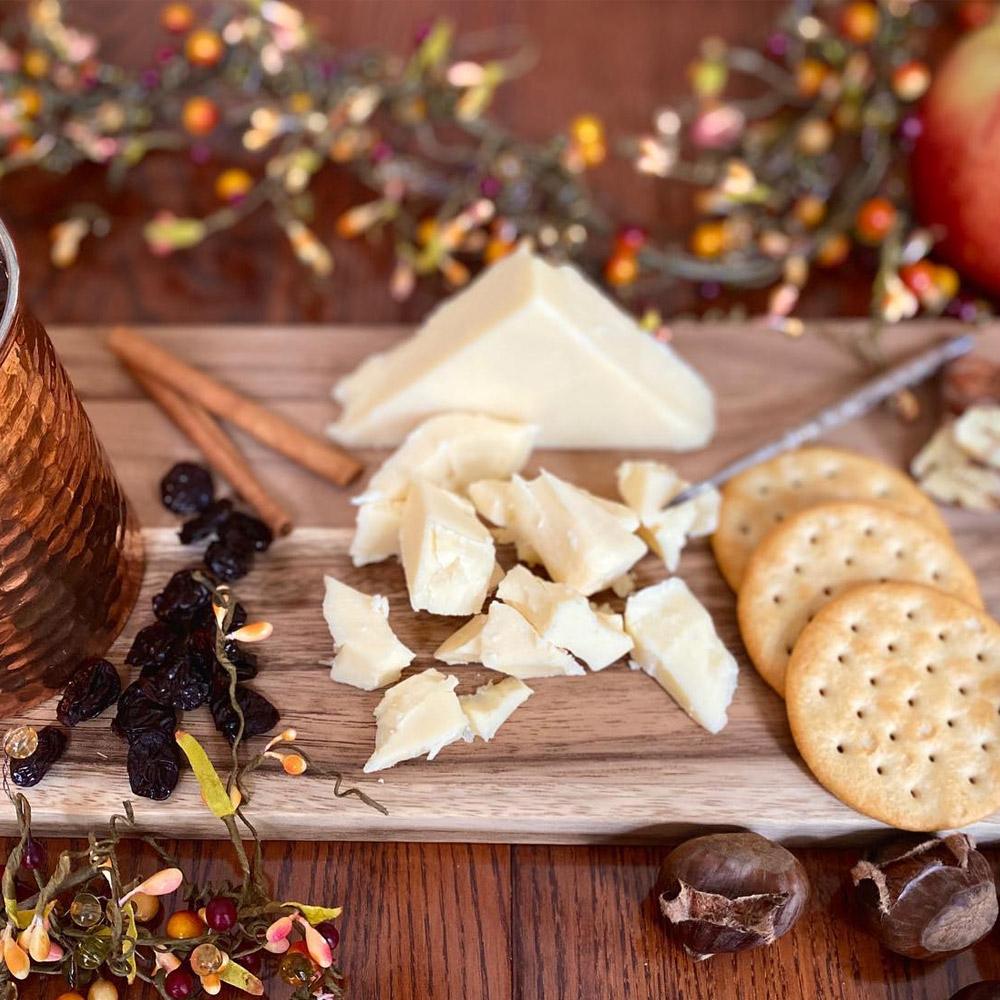 White chedddar cut into chunks on a cheese board with crackers and dried fruit next to a cider drink