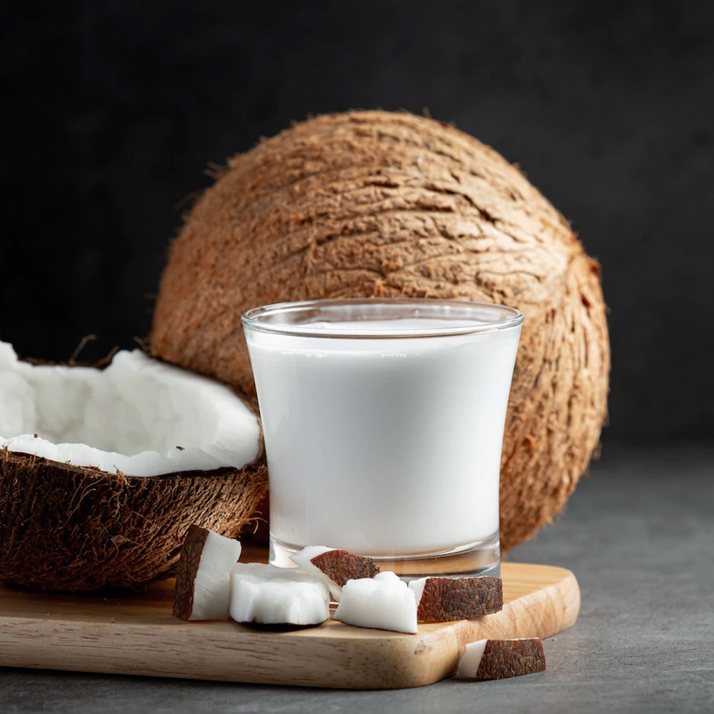 Glass of coconut milk on a wooden board next to a whole coconut and half coconut