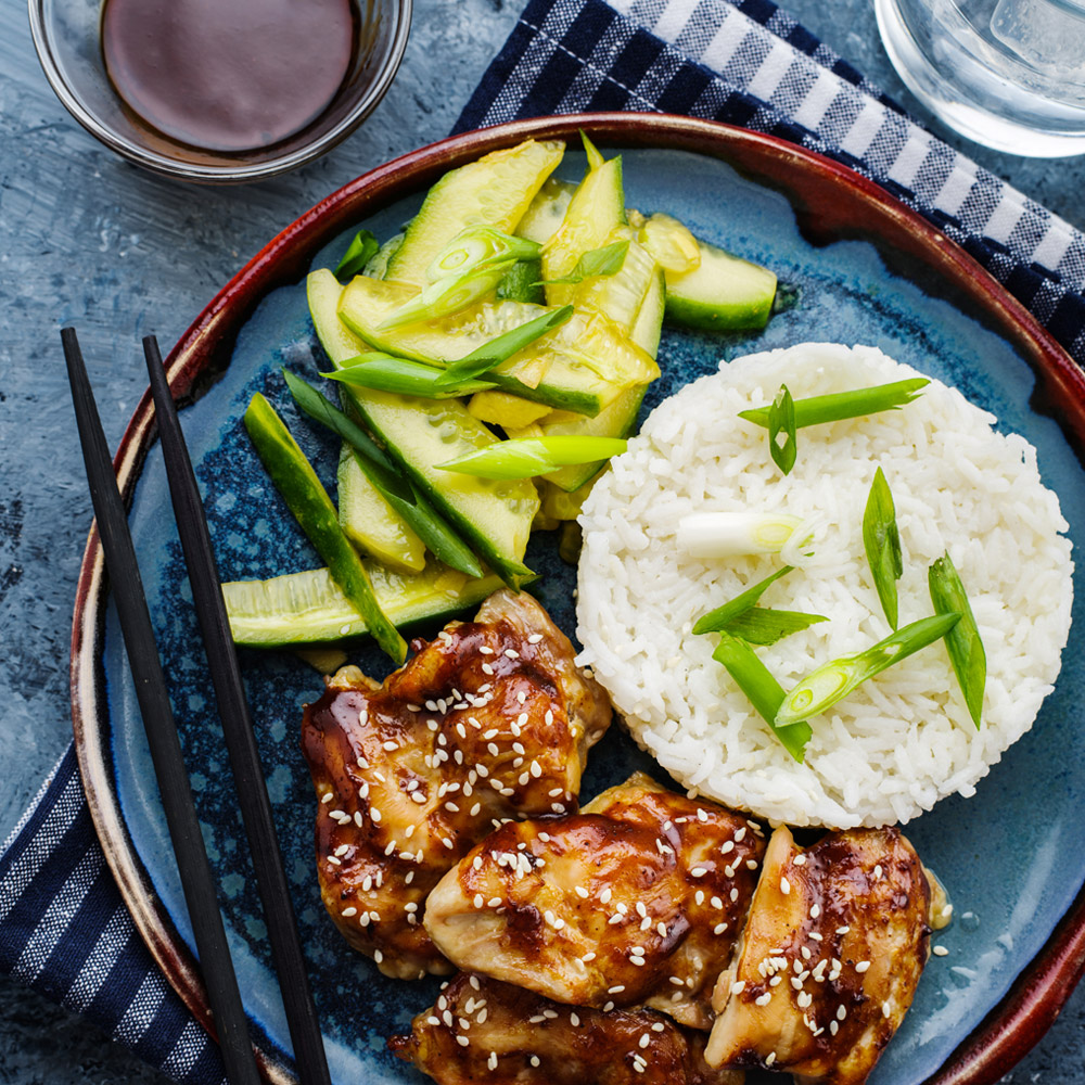 A bowl of hoisin sauce next to a plate with chicken rice and zucchini