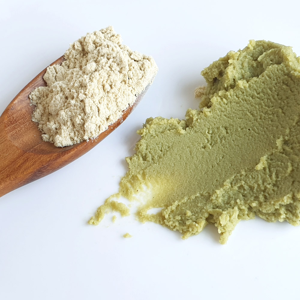 Wasabi powder on a wooden spoon next to a pile of wasabi paste