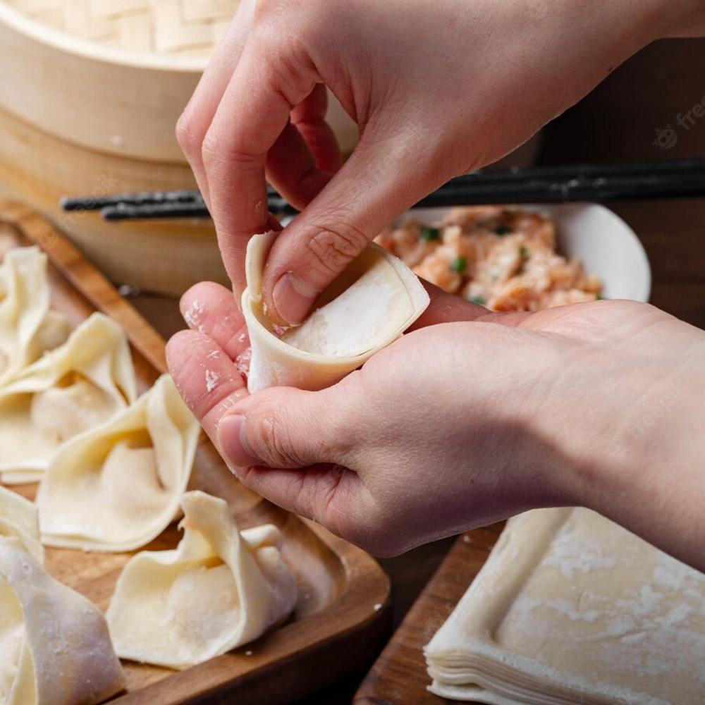 A chefs hands folding a wonton wrapper over a wooden board with wontons
