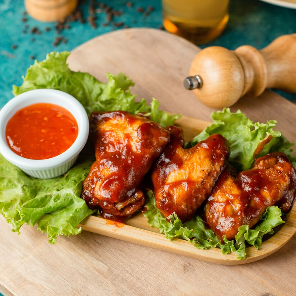 Chicken wings on a plate next to a bowl of chili sauce