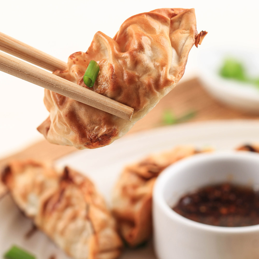 Gyoza asian potstickers with sauces served in brown ceramic japan style plate with chopsticks and spring onion over white wooden background