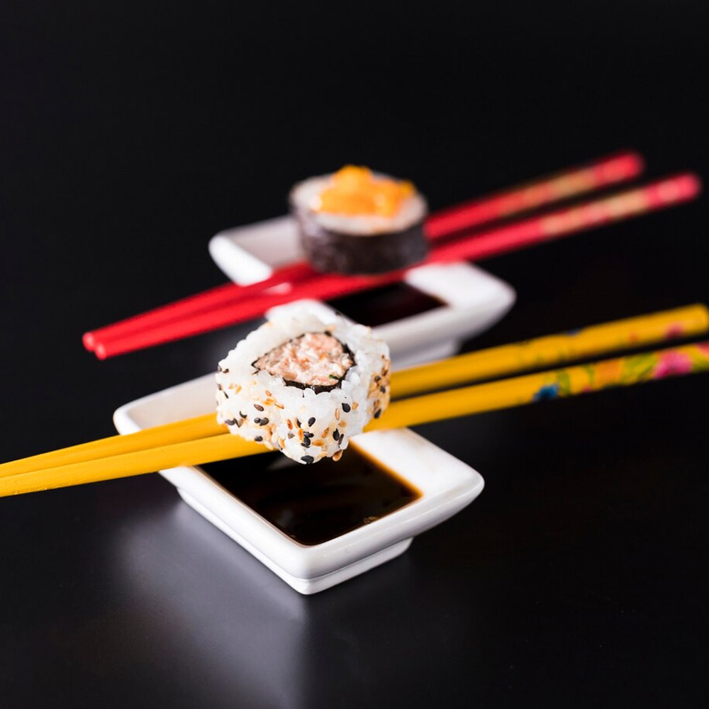 Sushi balancing on chopsticks over bowls of soy sauce