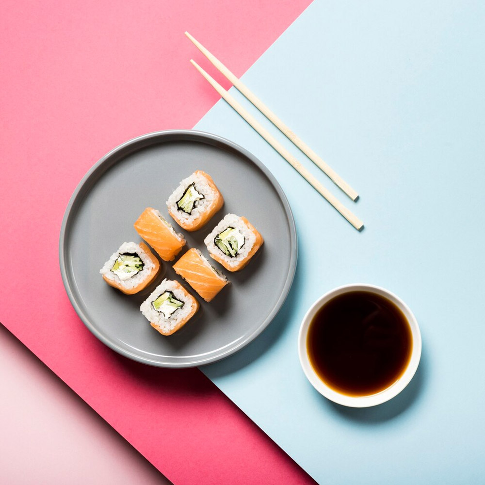 A bowl of soy sauce next to pieces of sushi and chopsticks