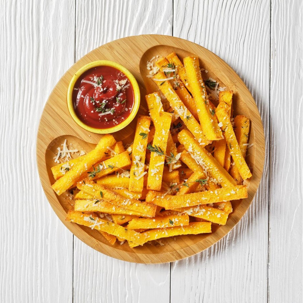 Garlic parmesan polenta fries with parmesan cheese, thyme and spices in a bamboo dish with tomato sauce on a white wooden table