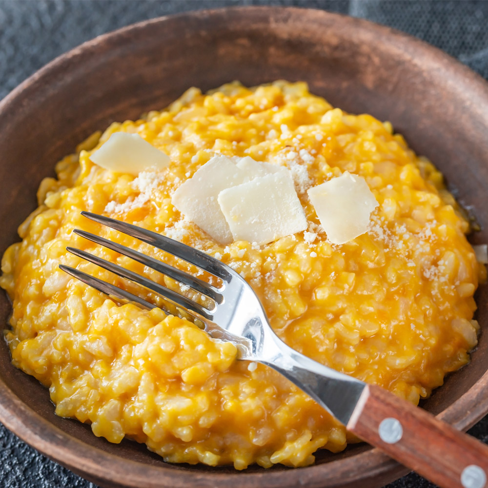 A bowl of pumpkin risotto with a fork and cheese on top