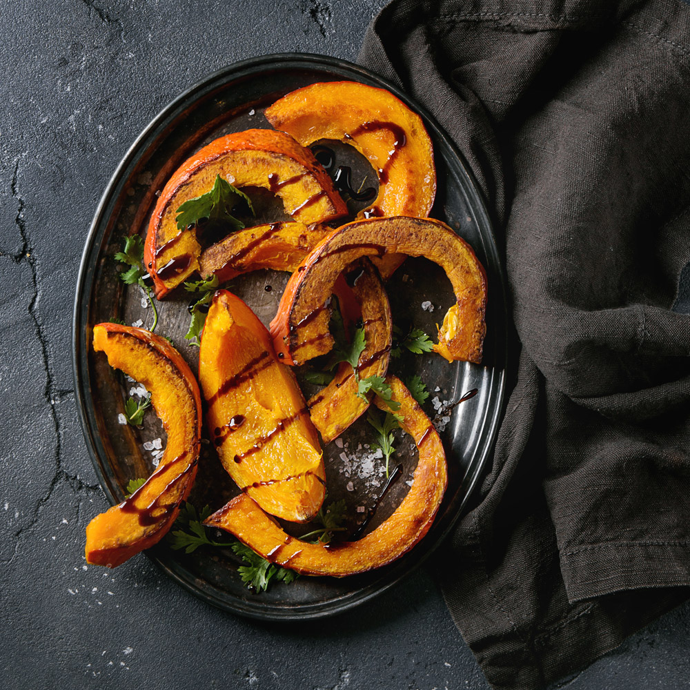 Slices of roasted pumpkin drizzled with balsamic glaze on a dark background