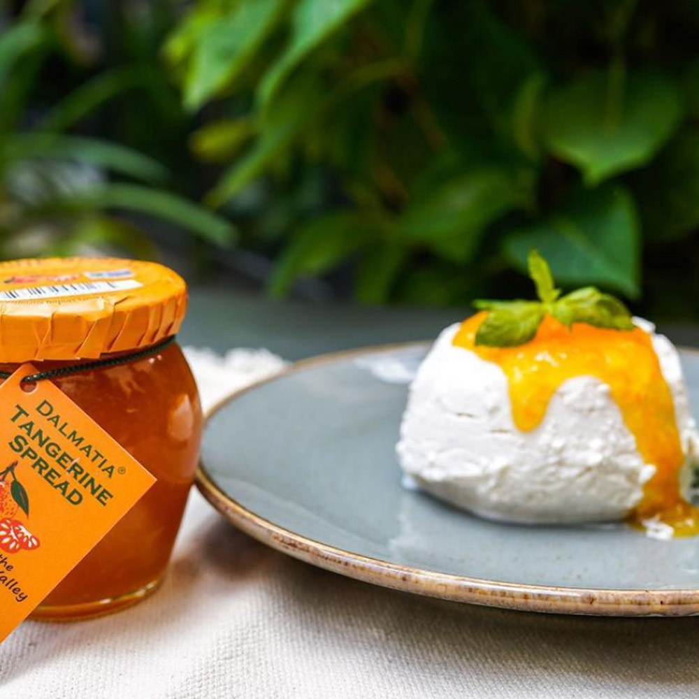 A jar of Dalmatia Tangerine Spread next to a puck of cheese topped with tangerine spread