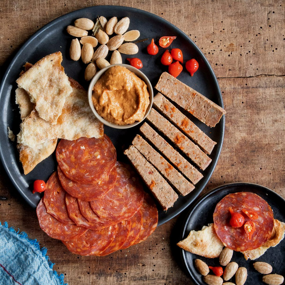 Slices of chorizo and pate on a plate with accoutrements
