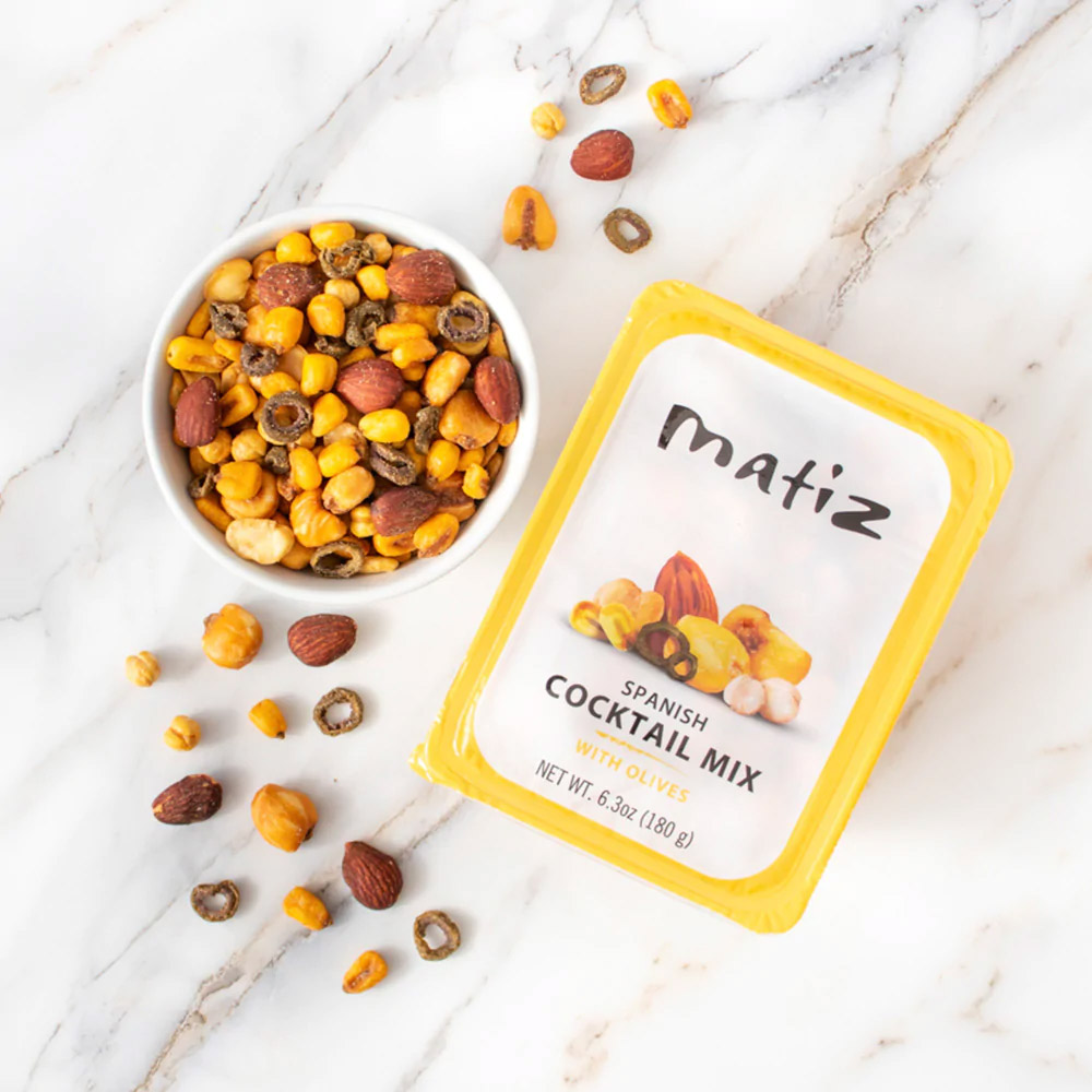 A container of Matiz Spanish Cocktail Mix with Olives next to a bowl of Matiz Spanish Cocktail Mix with Olives
