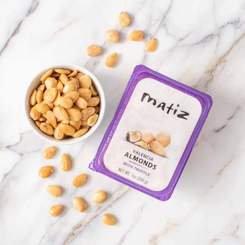 A container of Matiz Valencia Almonds with Truffle next to a bowl of Matiz Valencia Almonds with Truffle