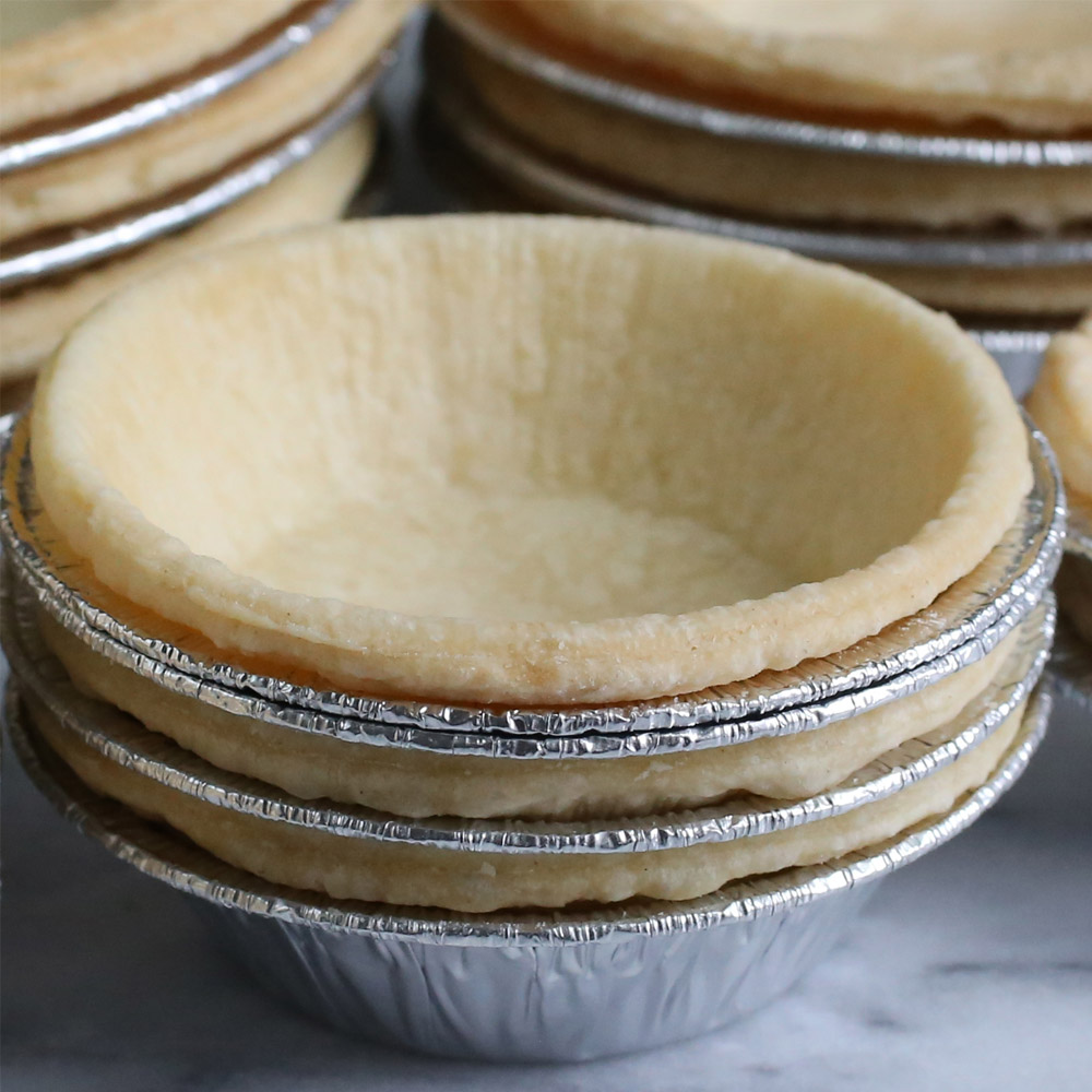 Dufour Pastry Kitchens 4 inch traditional tart shells in metal tins on a marble counter