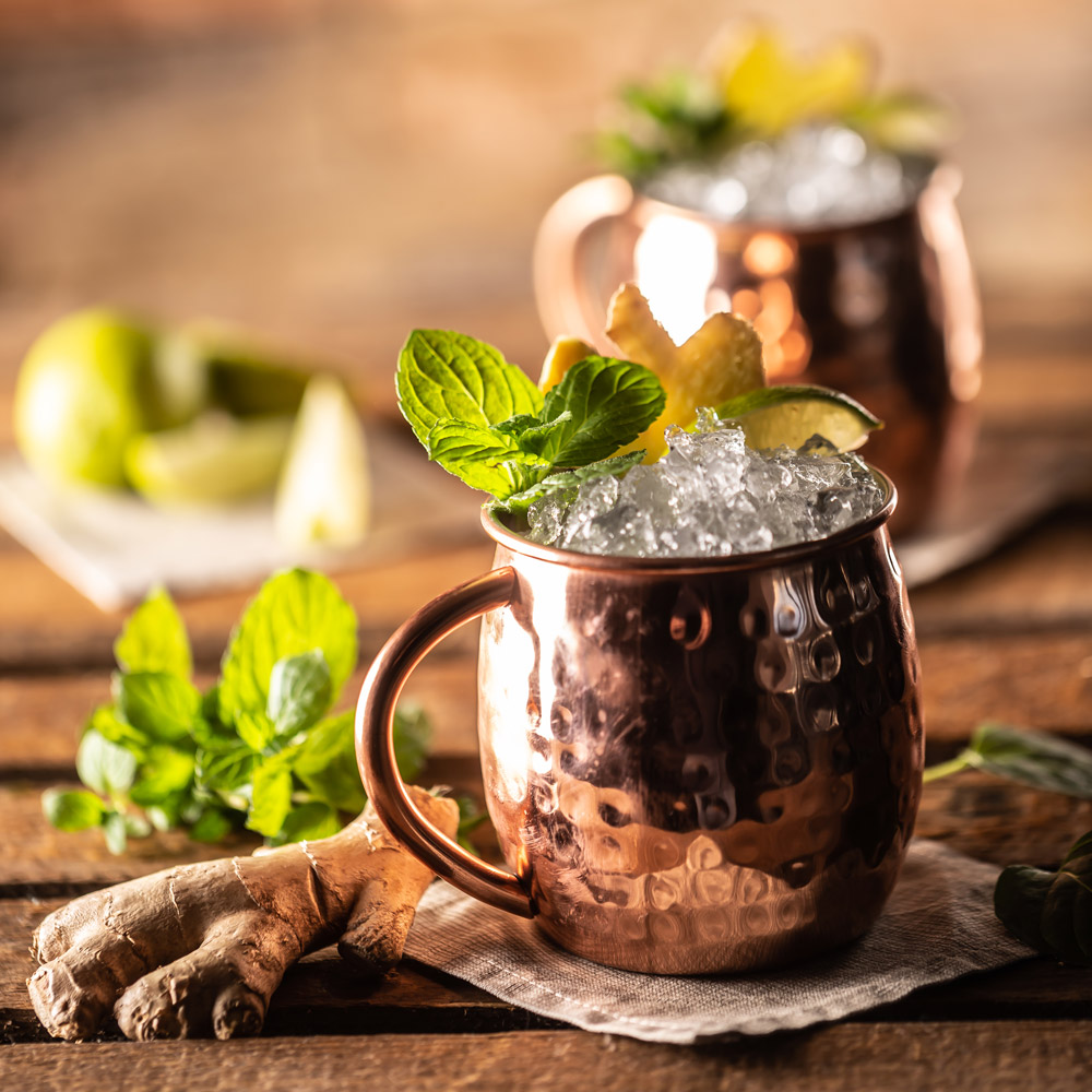 Two Moscow mules on a table with ice and ginger