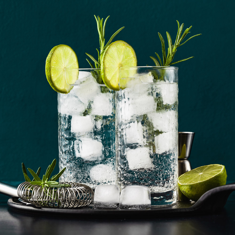 Classic gin and tonic cocktail with rosemary sprigs in tall glasses on a table with bar accessories