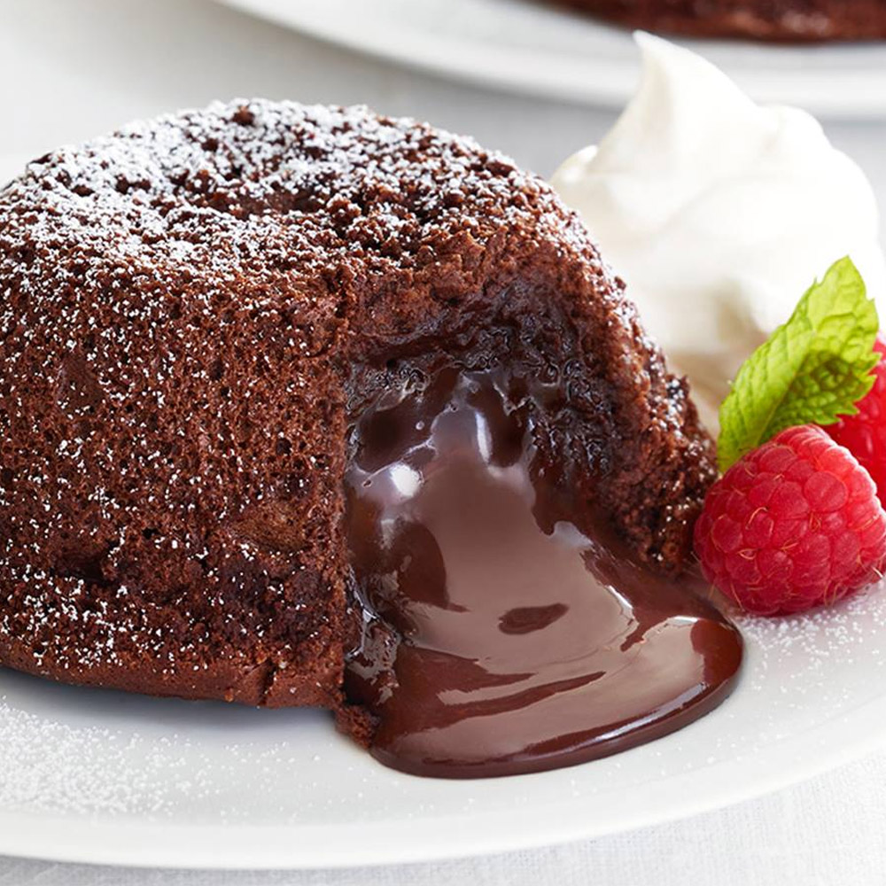 A chocolate lava cake cut open next to raspberries on a plate