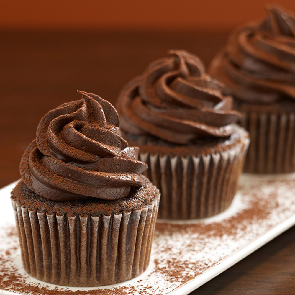 Three chocolate cupcakes on a plate sprinkled with cocoa powder