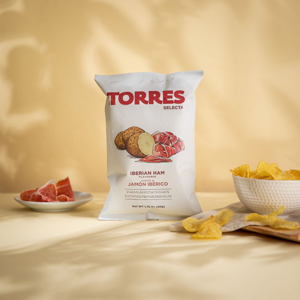 A bag of Torres potato chips on a table next to a bowl of chips