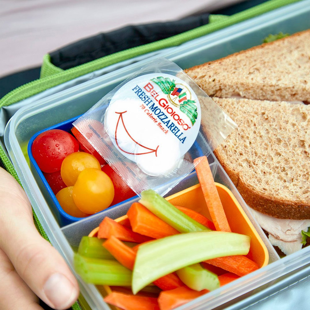 A small pack of BelGioioso mozzaralla in a lunch box with some cut vegetables and a sandwich