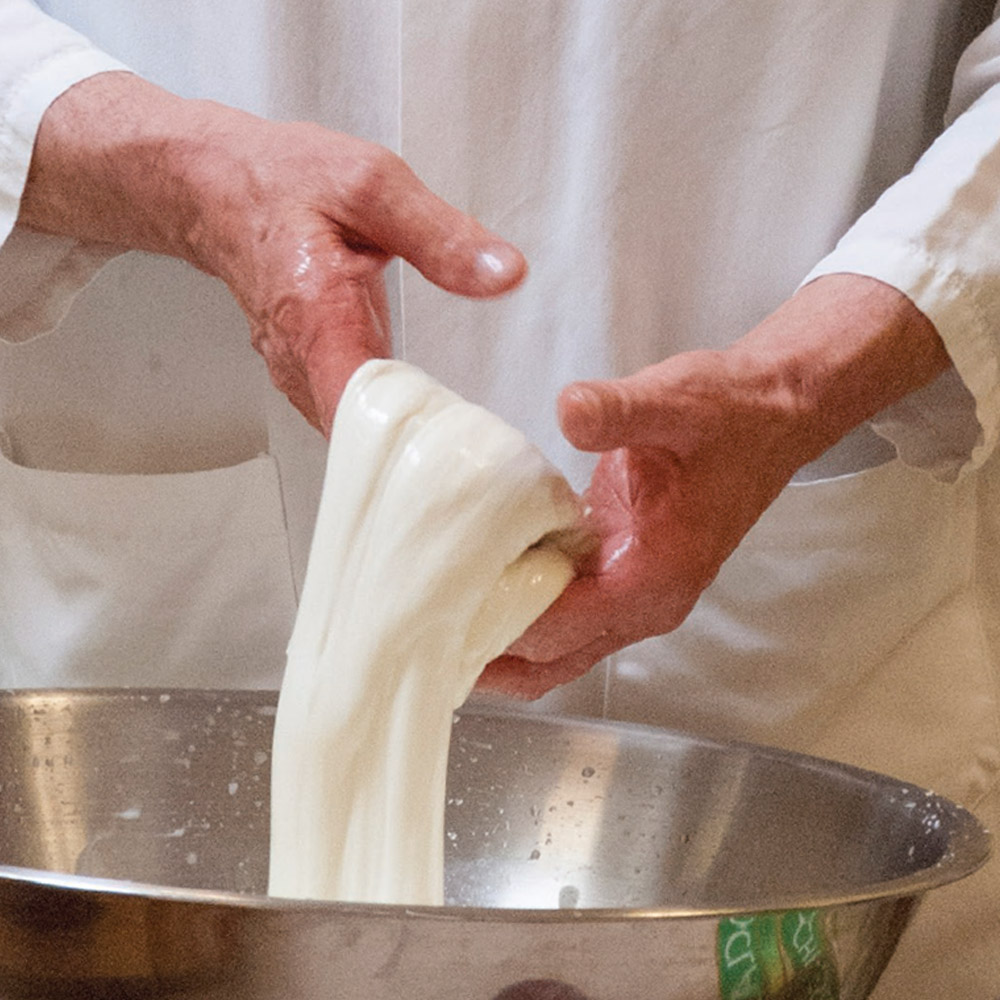 A man stretching fresh mozzarella curd over a silver bowl