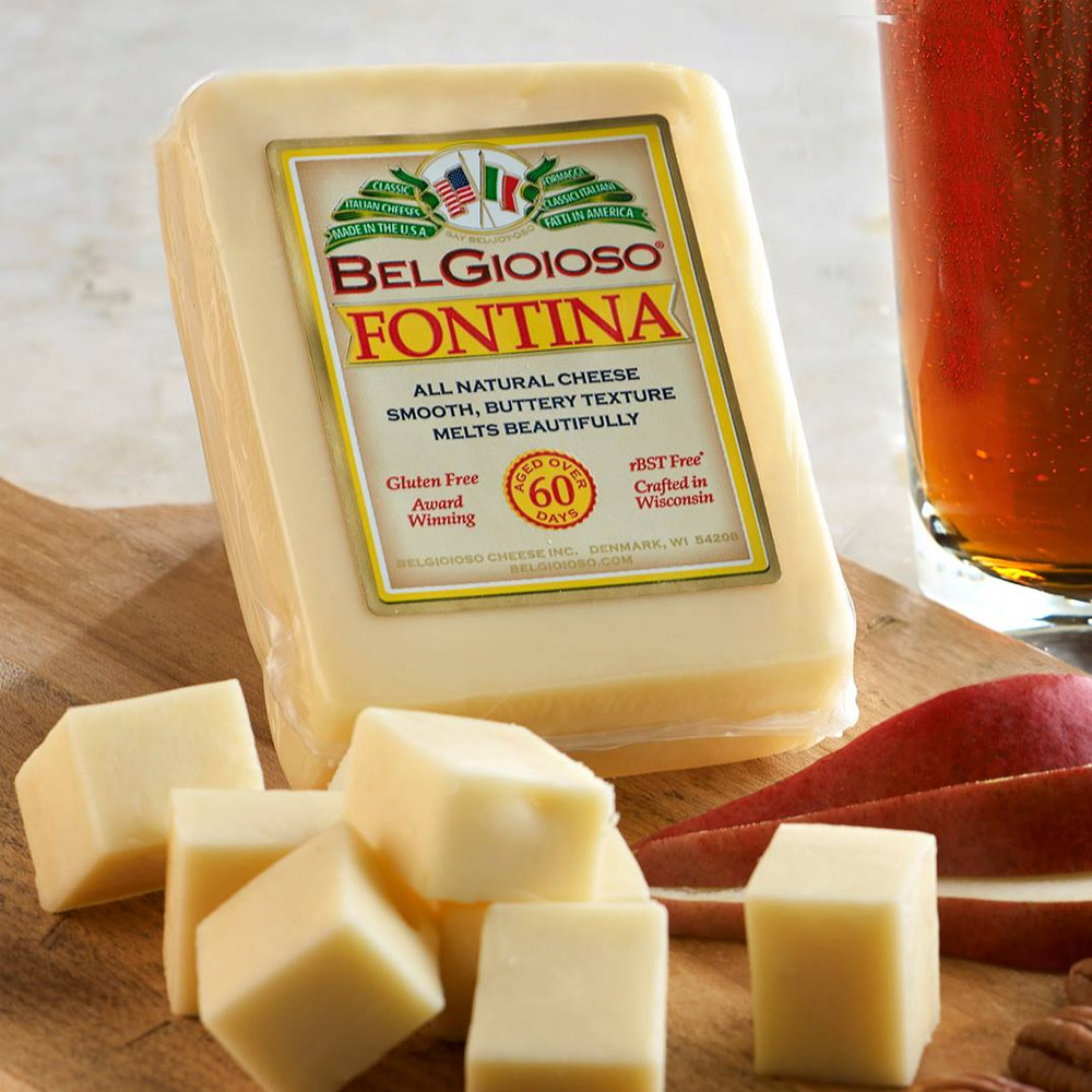 A wedge of Fontina cheese in the packaging on a wood board with apple slices and cubes of cheese