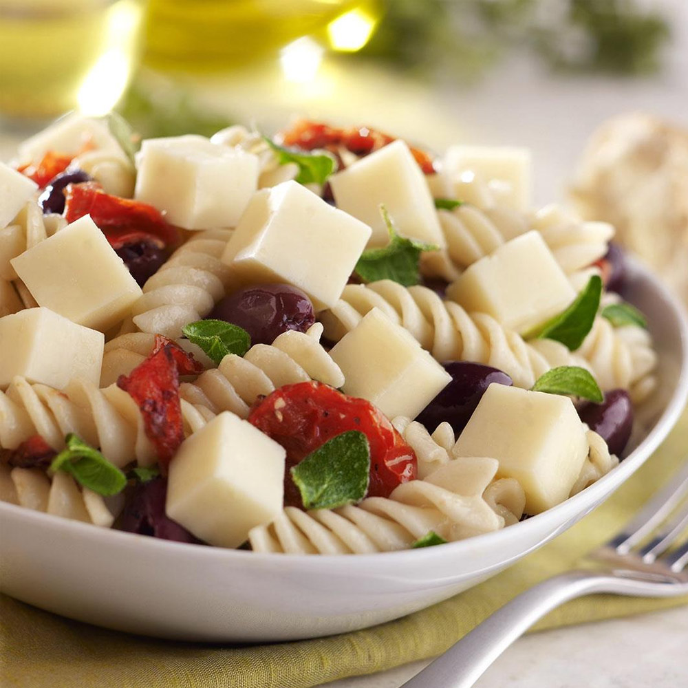 A close-up of pasta salad with cubes of cheese and pepperoni