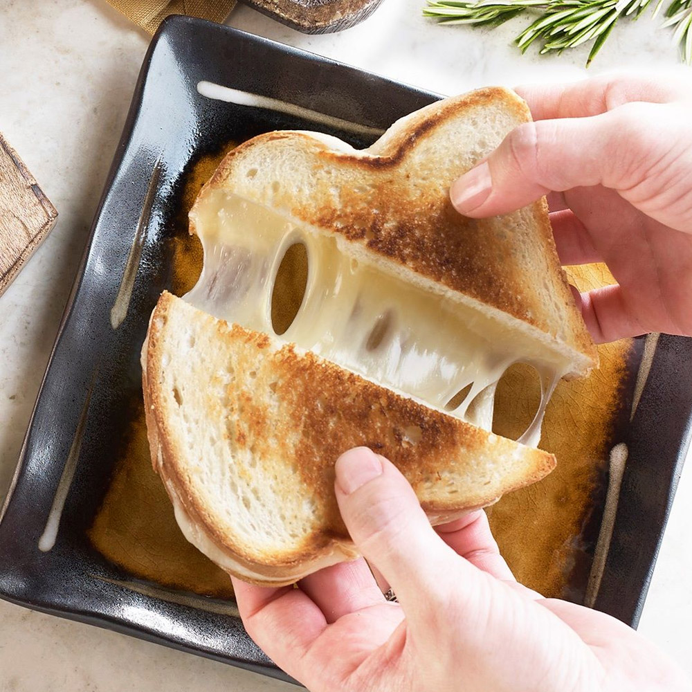 A grilled cheese sandwich being pulled apart over a plate