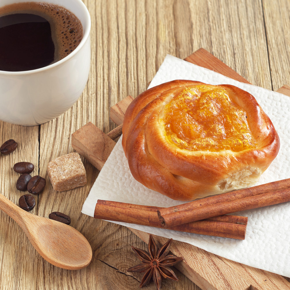Cup of hot coffee and bun with apricot jam on wooden table