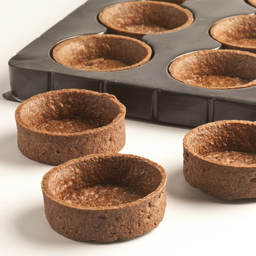 Moda chocolate round 1.9 inch tart shells in a tray with tart shells on a counter in front of the tray