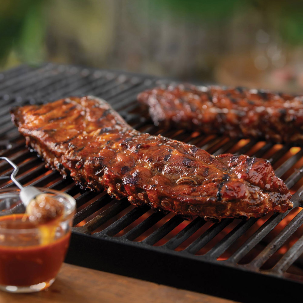 Cooked ribs on a grill grate with a cup of barbecue sauce