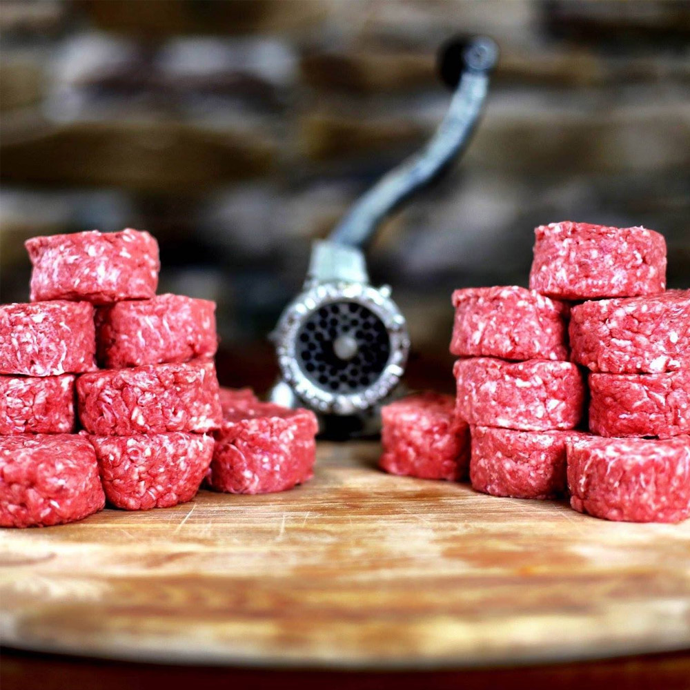 Ground meat patties and a meat grinder on a cutting board