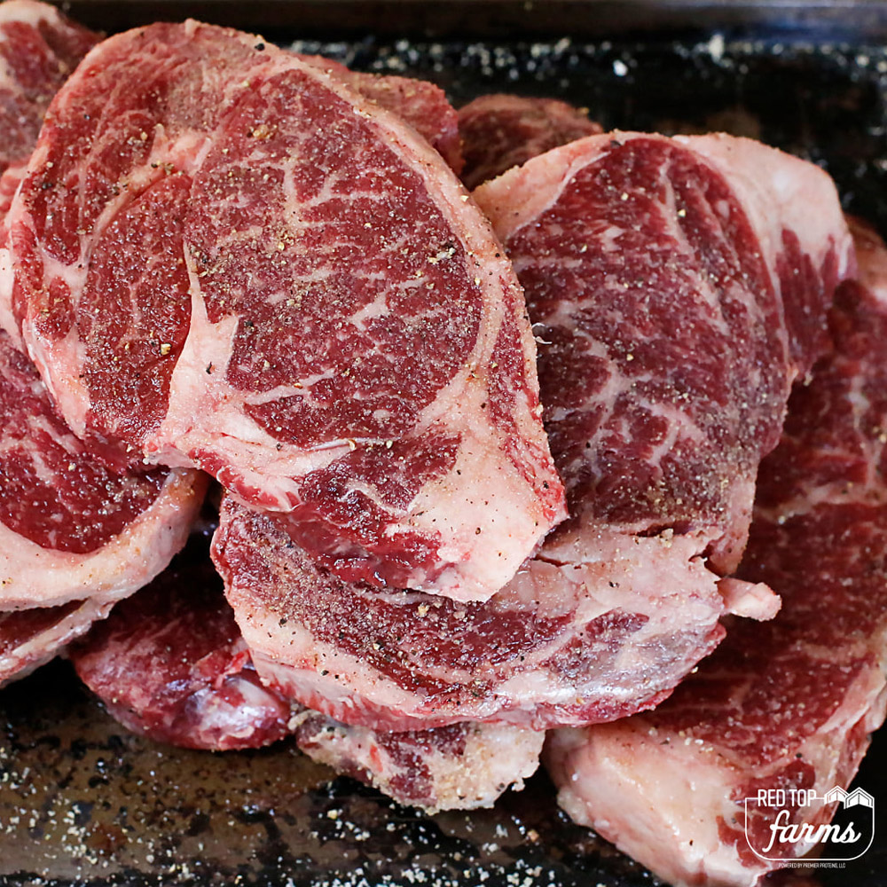 Raw beef steaks with seasonings on a slate board